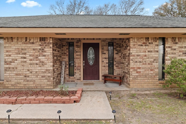 doorway to property featuring brick siding and a shingled roof