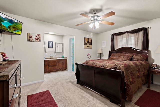 bedroom featuring light carpet, connected bathroom, a ceiling fan, and baseboards