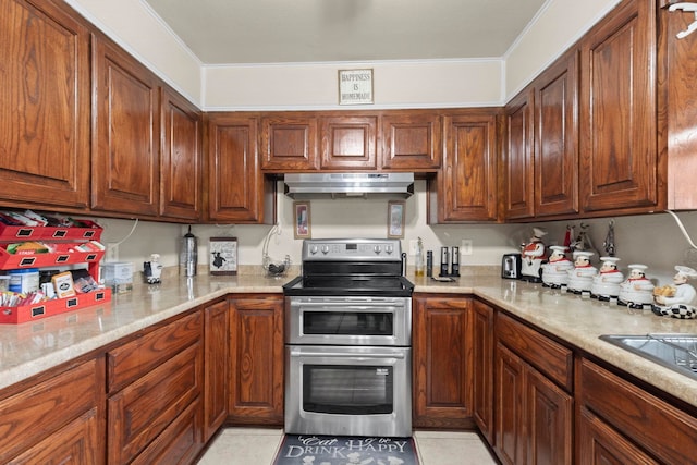 kitchen with ornamental molding, range with two ovens, under cabinet range hood, brown cabinetry, and light tile patterned floors