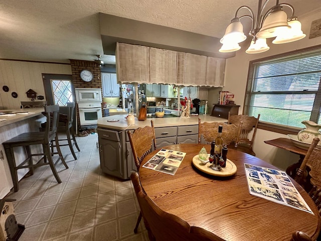 kitchen with a textured ceiling, a notable chandelier, white appliances, and hanging light fixtures