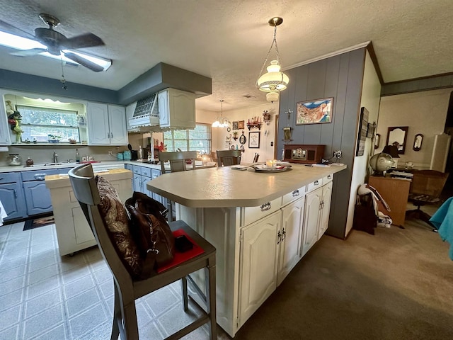 kitchen with a breakfast bar, a center island, white cabinets, hanging light fixtures, and a textured ceiling