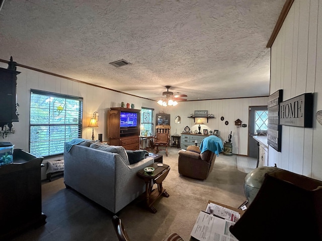 carpeted living room with a textured ceiling, ceiling fan, wood walls, and ornamental molding