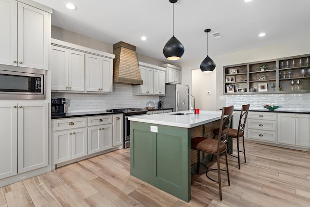 kitchen featuring wall chimney range hood, tasteful backsplash, pendant lighting, a kitchen island with sink, and appliances with stainless steel finishes