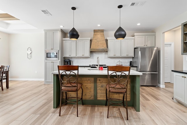 kitchen with wall chimney range hood, hanging light fixtures, appliances with stainless steel finishes, and a breakfast bar area