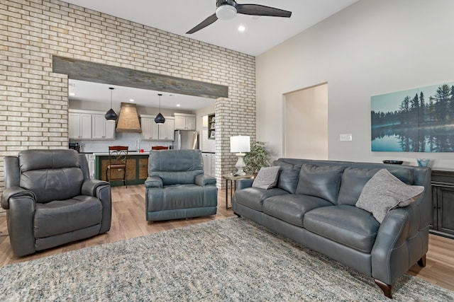 living room featuring ceiling fan, light hardwood / wood-style floors, and brick wall