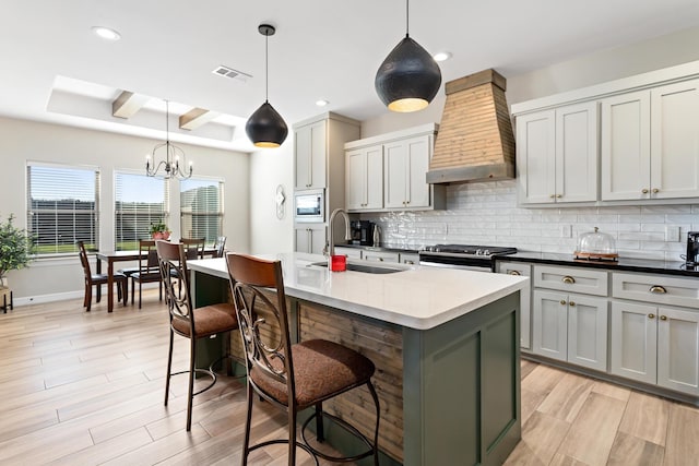 kitchen with appliances with stainless steel finishes, premium range hood, a kitchen island with sink, sink, and decorative light fixtures