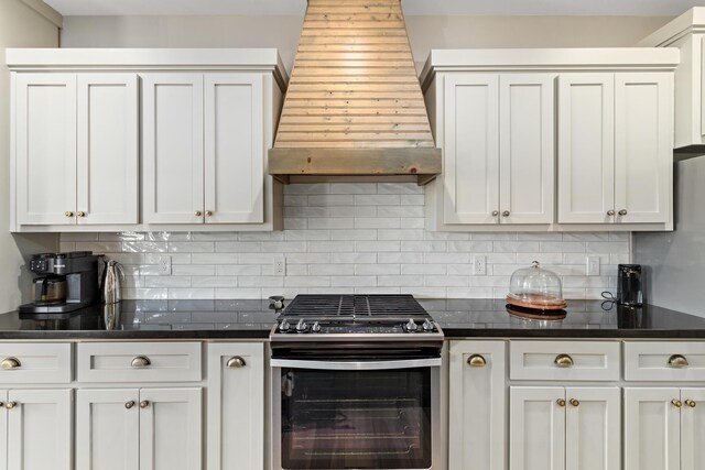 kitchen featuring stainless steel gas range oven, white cabinetry, premium range hood, and tasteful backsplash