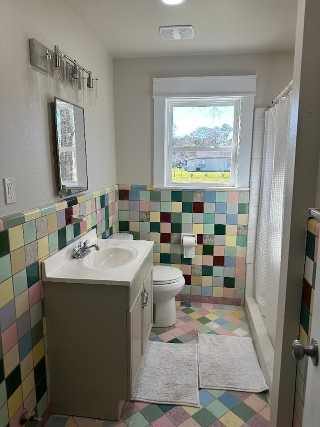 full bath with visible vents, a wainscoted wall, toilet, vanity, and tile walls