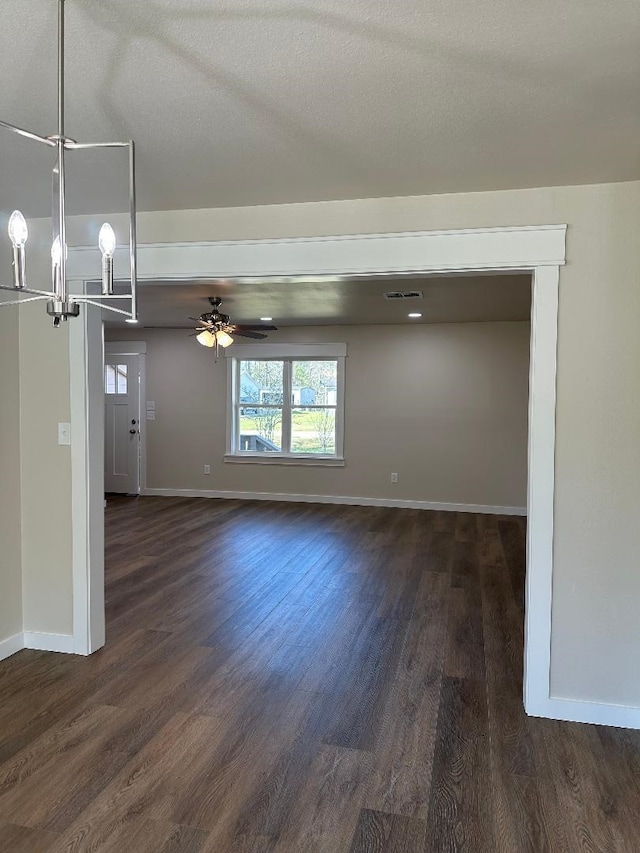 unfurnished room featuring dark wood-style floors, ceiling fan with notable chandelier, a textured ceiling, and baseboards