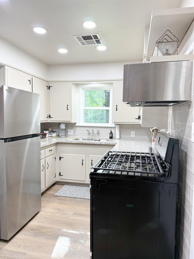 6744 Keith Rd, Lumberton, TX 77657 - kitchen with freestanding refrigerator, black range with gas cooktop, light wood-style floors, white cabinets, and recessed lighting