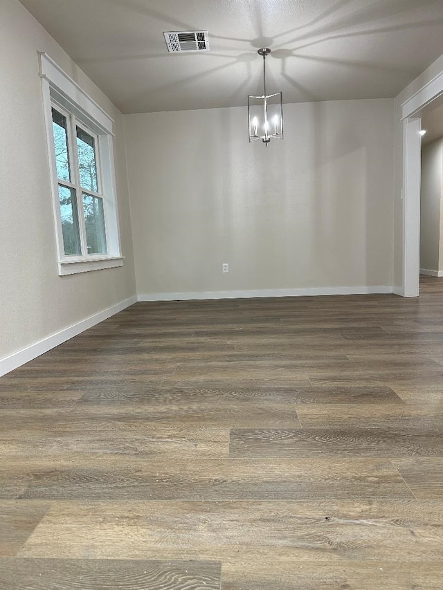 empty room with visible vents, baseboards, an inviting chandelier, and wood finished floors