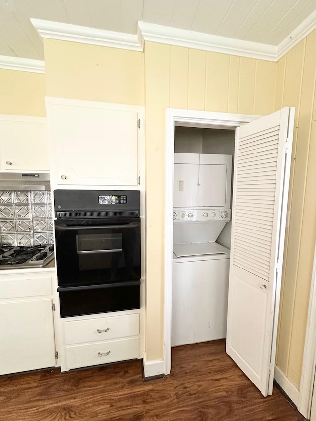 kitchen featuring ornamental molding, stainless steel gas cooktop, stacked washer and clothes dryer, white cabinets, and black oven