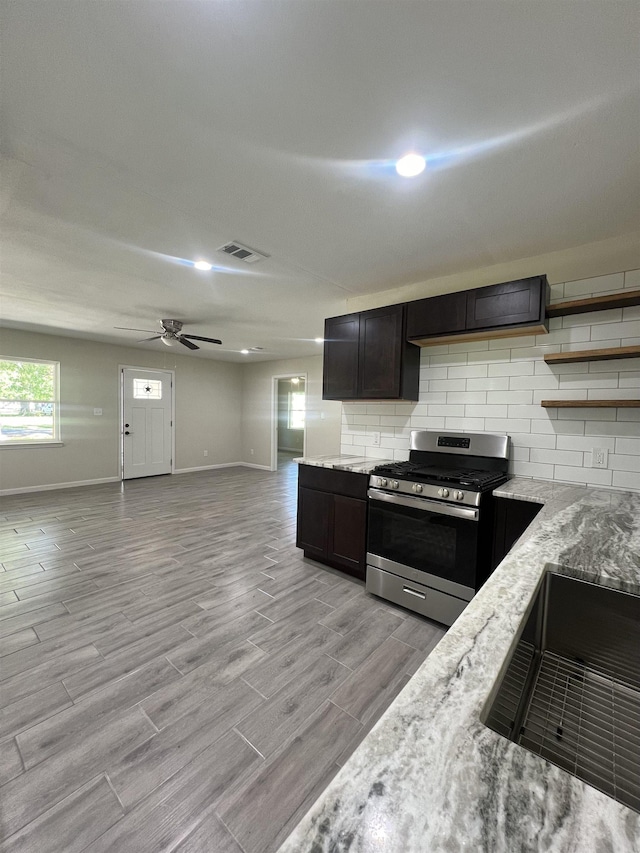 kitchen with light stone countertops, decorative backsplash, dark brown cabinetry, ceiling fan, and stainless steel gas stove