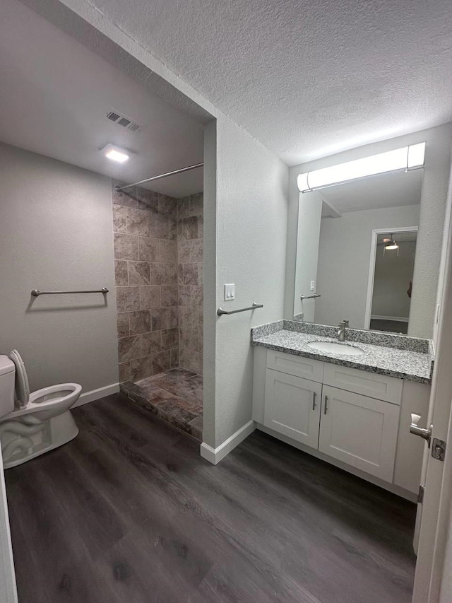 bathroom with vanity, hardwood / wood-style flooring, toilet, tiled shower, and a textured ceiling