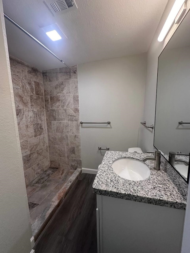 bathroom featuring a tile shower, hardwood / wood-style floors, a textured ceiling, toilet, and vanity