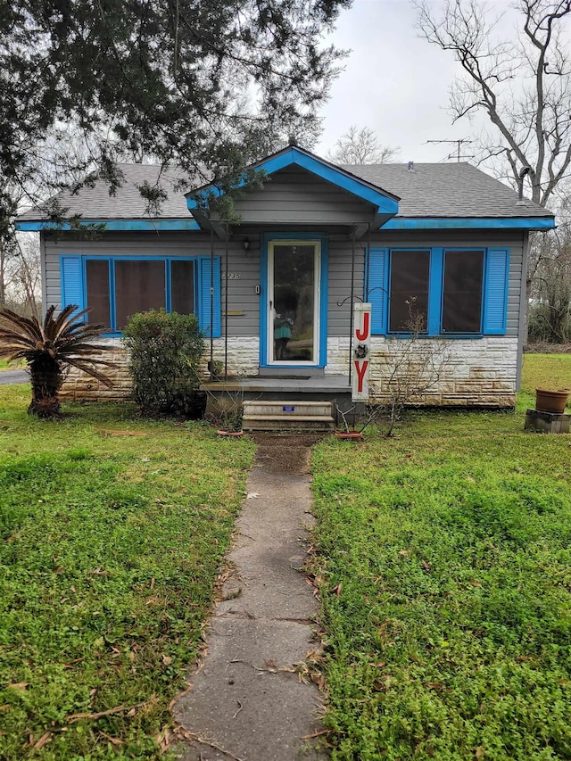 view of front of property with stone siding, roof with shingles, and a front lawn