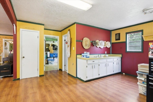 kitchen featuring white cabinets, sink, crown molding, light hardwood / wood-style flooring, and a textured ceiling