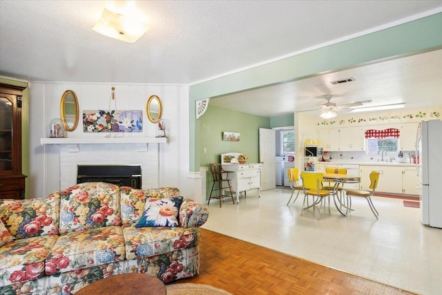 living room featuring a brick fireplace, parquet floors, a textured ceiling, ceiling fan, and washer / dryer