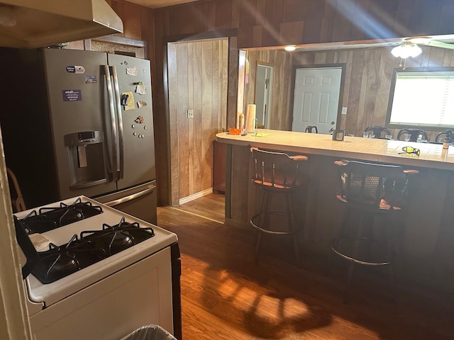 kitchen with wood walls, a kitchen breakfast bar, white gas range oven, dark hardwood / wood-style floors, and stainless steel fridge with ice dispenser