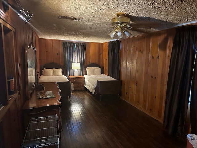 bedroom featuring a textured ceiling, wooden walls, ceiling fan, and dark hardwood / wood-style floors