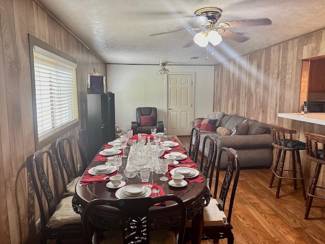 dining room featuring a textured ceiling, hardwood / wood-style flooring, ceiling fan, and wooden walls