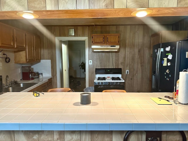 kitchen with gas range gas stove, tile counters, sink, stainless steel fridge with ice dispenser, and decorative backsplash