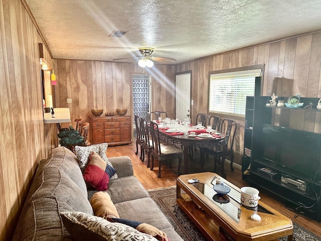 living room with ceiling fan, wooden walls, hardwood / wood-style floors, and a textured ceiling