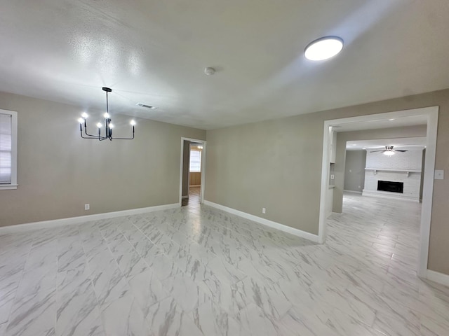 spare room featuring a large fireplace and ceiling fan with notable chandelier