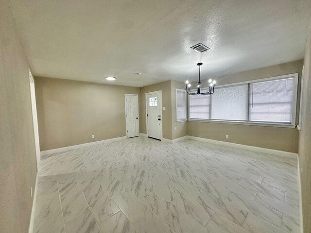 empty room with an inviting chandelier, a wealth of natural light, and a textured ceiling