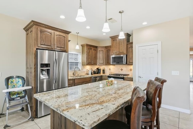 kitchen with pendant lighting, sink, appliances with stainless steel finishes, a center island, and light stone countertops