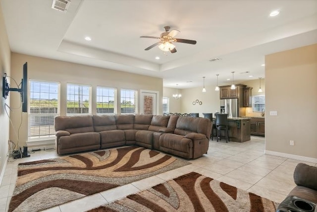 tiled living room with a raised ceiling and ceiling fan with notable chandelier