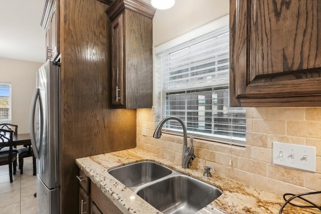 kitchen featuring sink, stainless steel refrigerator, backsplash, light stone countertops, and light tile patterned flooring