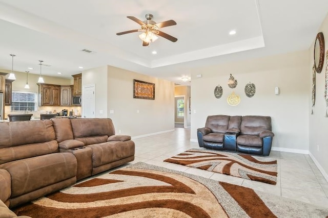 living room with ceiling fan, a tray ceiling, and light tile patterned floors