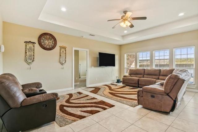 living room featuring a raised ceiling, ceiling fan, and light tile patterned flooring