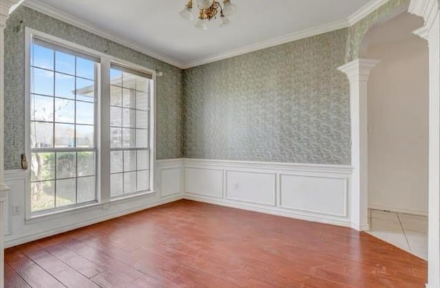 empty room featuring ornamental molding, arched walkways, decorative columns, and wallpapered walls