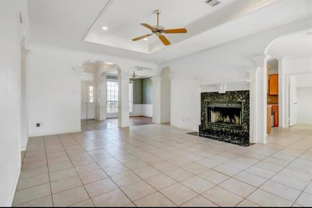 unfurnished living room with arched walkways, light tile patterned flooring, a fireplace, a ceiling fan, and a tray ceiling