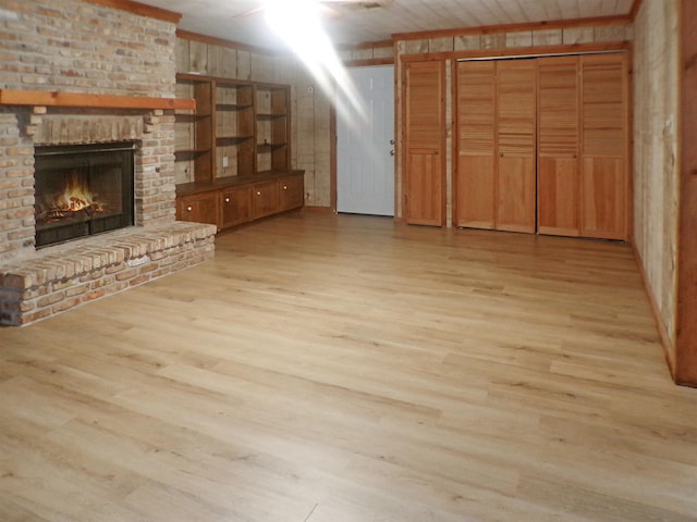 unfurnished living room featuring wooden walls, light wood-type flooring, and a brick fireplace