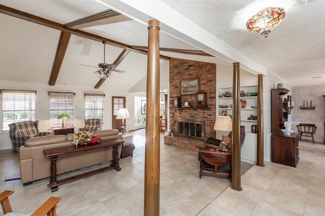 living room featuring ceiling fan, a brick fireplace, vaulted ceiling with beams, a textured ceiling, and ornate columns