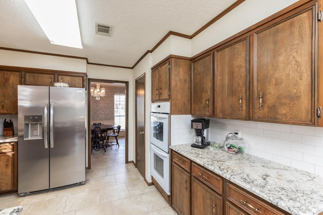 kitchen featuring stainless steel fridge, decorative backsplash, a textured ceiling, double oven, and light stone counters