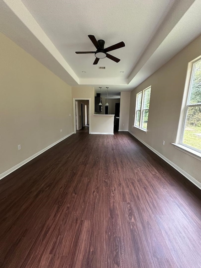 unfurnished living room featuring a textured ceiling, dark hardwood / wood-style flooring, a raised ceiling, and ceiling fan