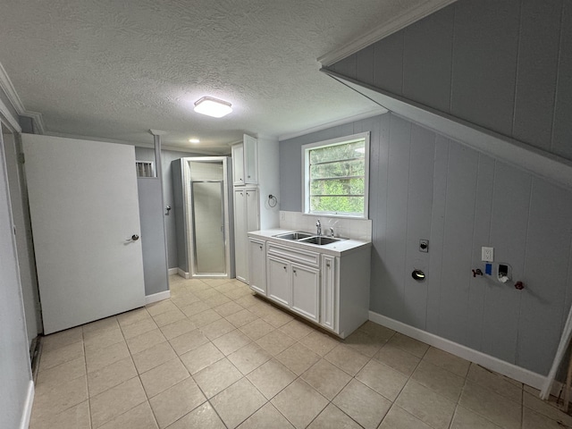 clothes washing area featuring wood walls, cabinets, sink, a textured ceiling, and light tile patterned flooring