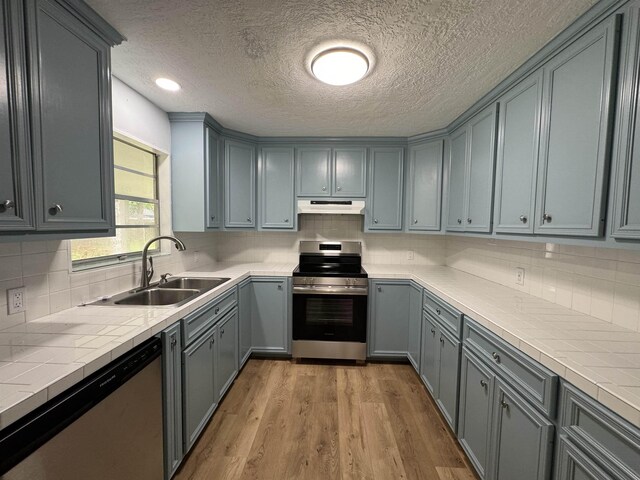 kitchen featuring stainless steel appliances, sink, tile countertops, light hardwood / wood-style flooring, and gray cabinets