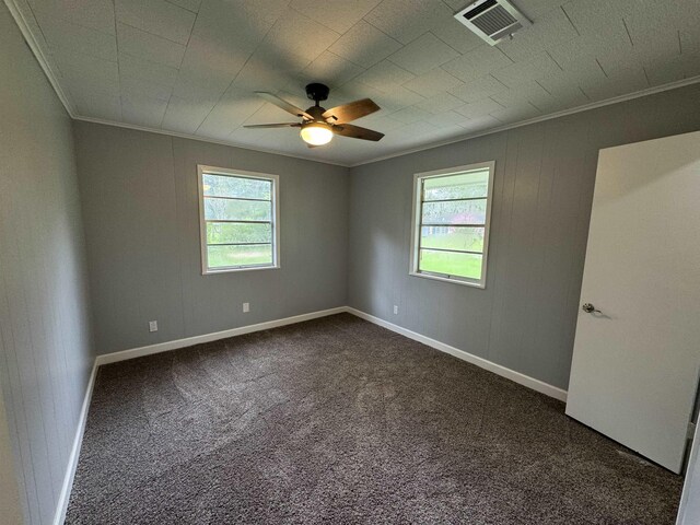 unfurnished room with ornamental molding, a healthy amount of sunlight, and dark carpet