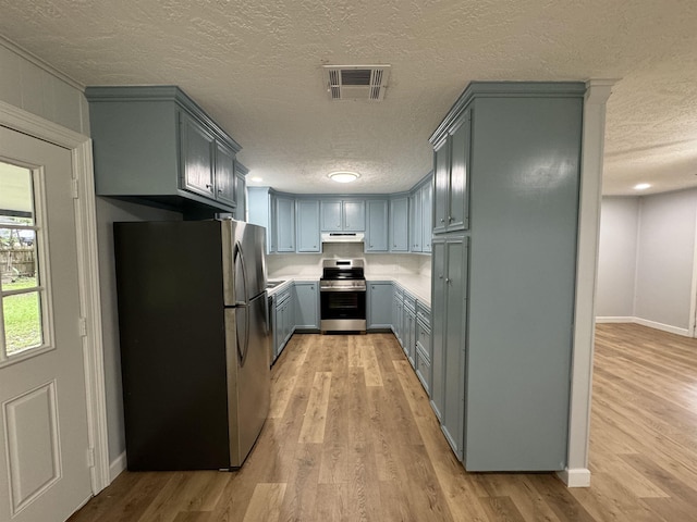 kitchen featuring light wood-type flooring, a textured ceiling, and appliances with stainless steel finishes