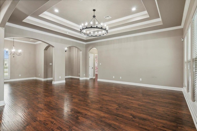 empty room with dark hardwood / wood-style flooring, a raised ceiling, ornamental molding, and a chandelier