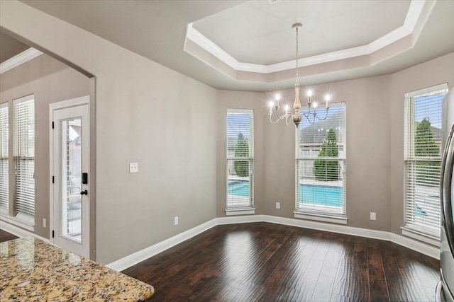 unfurnished dining area with ornamental molding, an inviting chandelier, a raised ceiling, and dark wood-type flooring