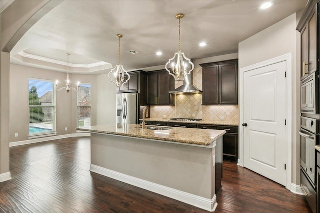 kitchen with dark brown cabinetry, stainless steel appliances, a tray ceiling, sink, and a center island with sink