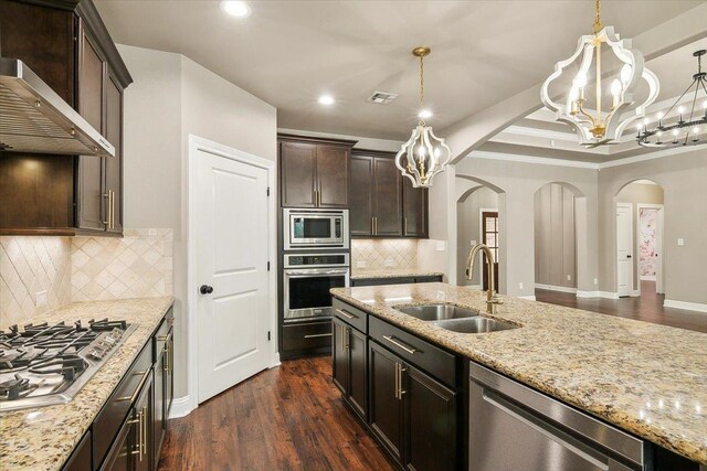 kitchen with wall chimney range hood, decorative light fixtures, stainless steel appliances, and sink