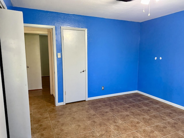 spare room featuring dark tile patterned floors, a textured wall, baseboards, and ceiling fan