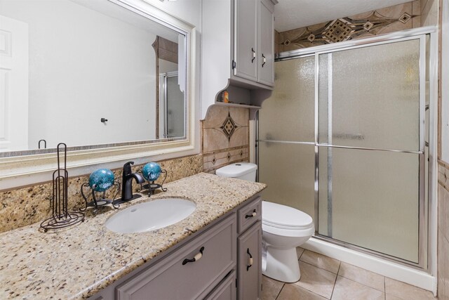 bathroom with tile patterned flooring, a shower with door, vanity, and toilet